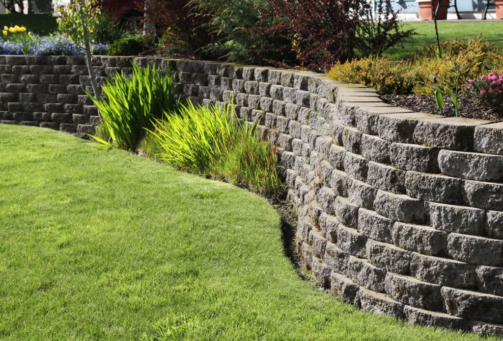 A garden with grass and bushes next to a stone wall.