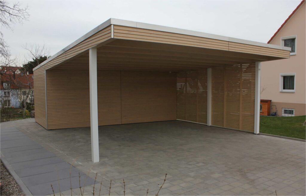 A wooden carport with white posts and concrete floor.